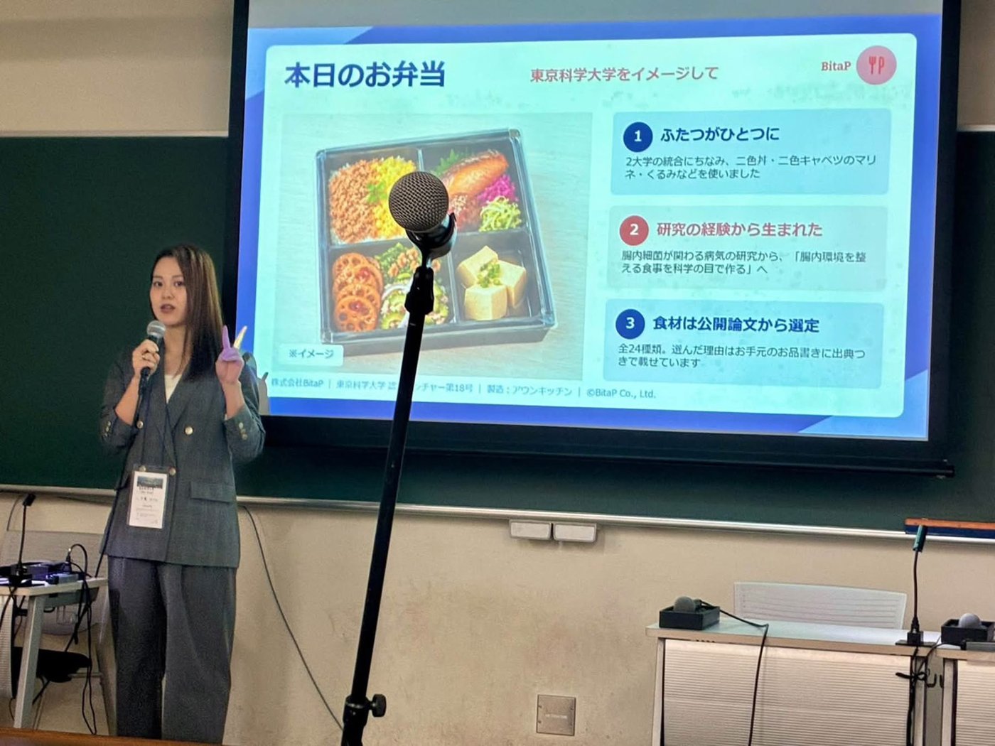 「本日のお弁当」のスライドを示しながら、お弁当を紹介する代表 千葉